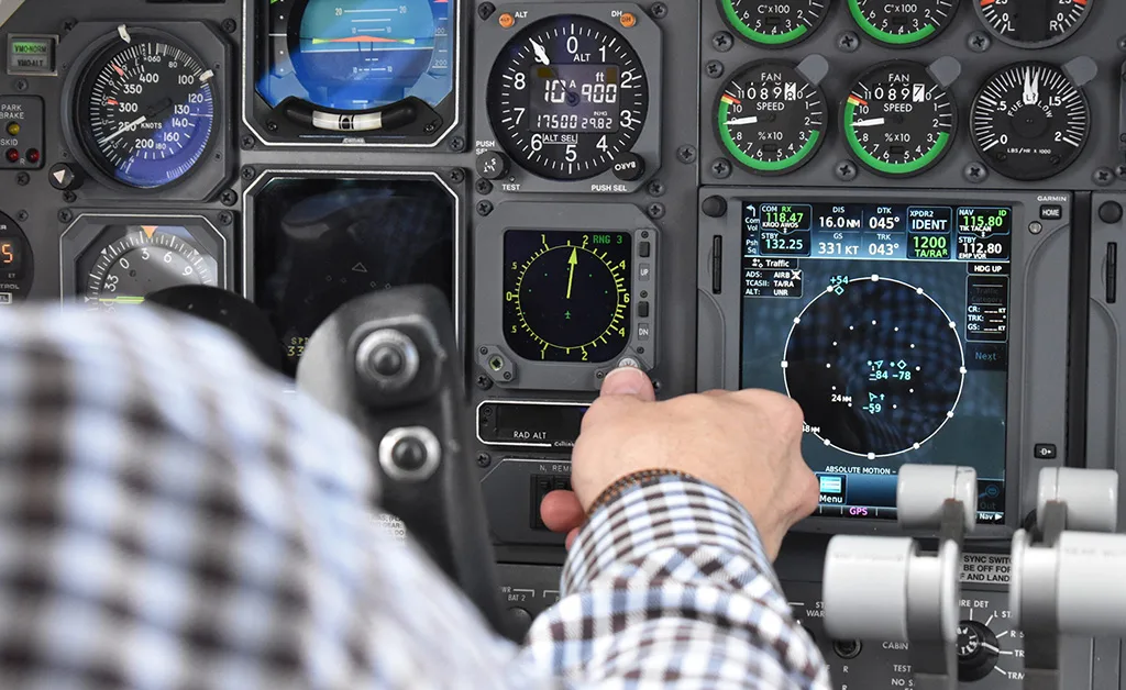 Close-up of a pilot adjusting controls on an avionics panel with a Garmin navigation system.