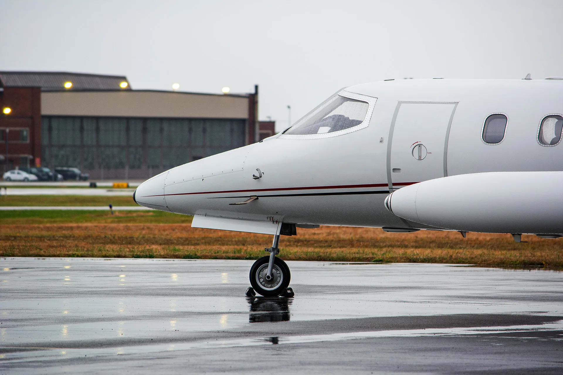 Side view of the front section of a Learjet parked on a wet, with a hangar and buildings in the background.