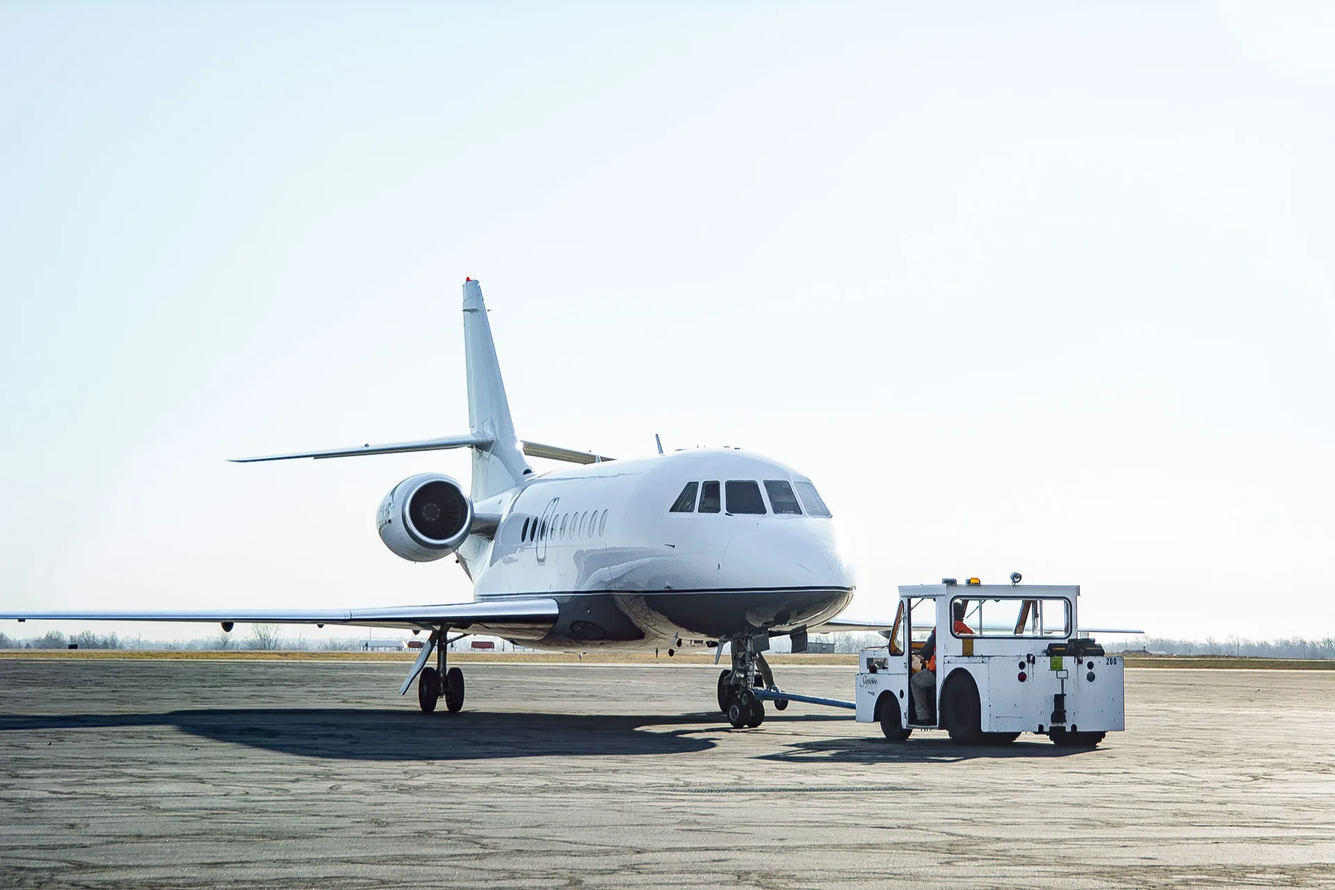 Large private aircraft being towed on the tarmac by a ground vehicle under clear skies.